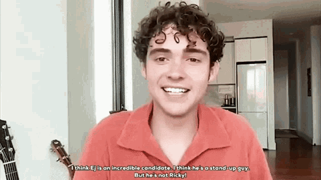 a young man with curly hair is standing in a living room with a guitar in front of him .