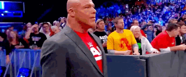a bald man in a suit and red shirt is standing in front of a crowd of people .