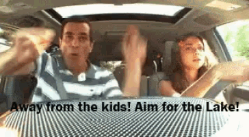 a man and a woman are driving a car and the woman is waving her hands .