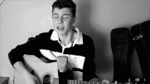a young man singing into a microphone while holding a guitar