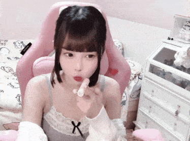 a girl is sitting in a pink chair and holding a tube of lipstick