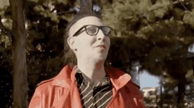 a man wearing glasses and a red jacket is standing in a park .