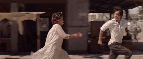 a man and a woman are running down a street and the woman is wearing a white dress .