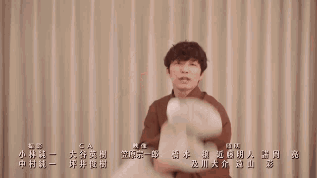 a man in a brown shirt is holding a white object with chinese writing on the bottom