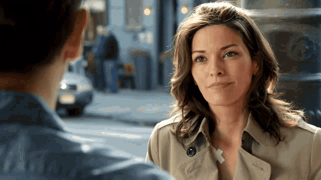a woman in a trench coat talks to a man