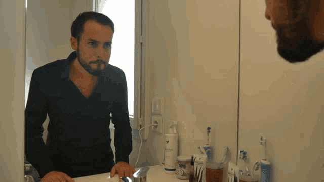 a man in a black shirt looks at himself in the mirror