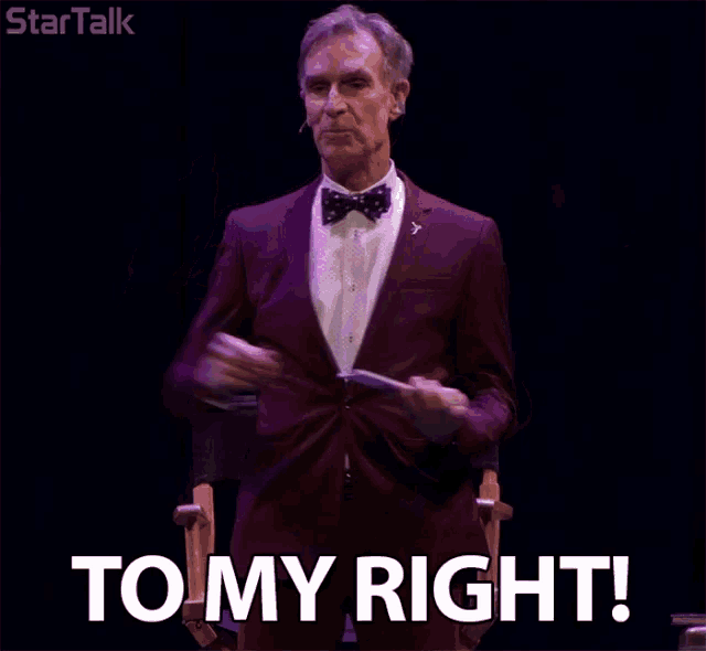 a man in a suit and bow tie holds a piece of paper and says to my right