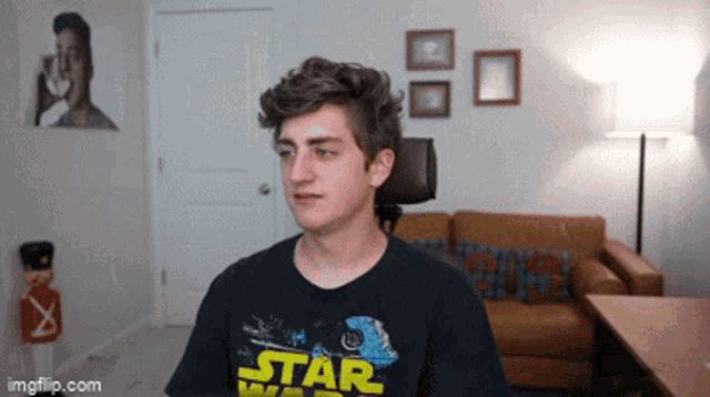 a young man wearing a black star wars shirt stands in a living room