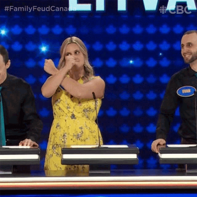 a woman in a yellow dress is standing in front of a microphone on a family feud game show .