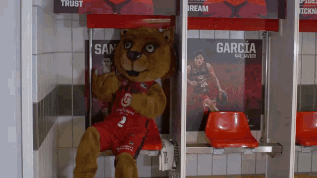 a mascot is sitting in a locker room with a poster of garcia on the wall