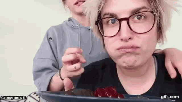 a woman wearing glasses is making a funny face while holding a spoon in her mouth .