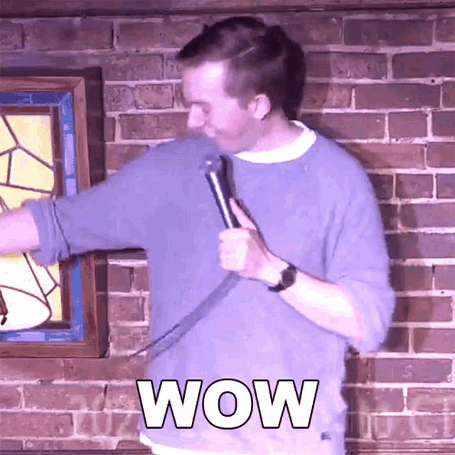 a man holding a microphone in front of a brick wall with the word wow on it