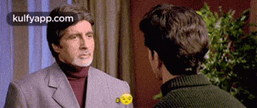 a man in a suit and turtleneck is talking to another man in a sweater .