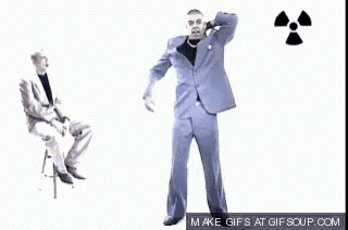 a man in a suit is dancing in front of a man sitting in a chair