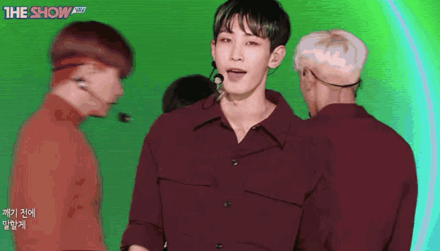 a man in a red shirt stands in front of a green screen that says the show on it