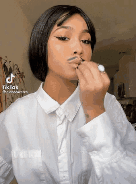 a woman wearing a white shirt and a ring is applying makeup on her lips