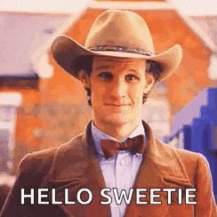 a man wearing a cowboy hat and bow tie is standing in front of a building and says `` hello sweetie '' .