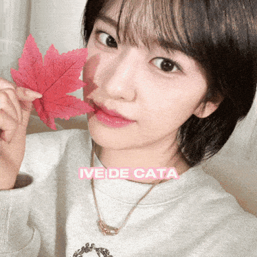 a woman holding a red maple leaf in front of her face with the name ive de cata on the bottom right