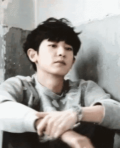 a young man is sitting in a chair with his hands folded and looking at the camera .