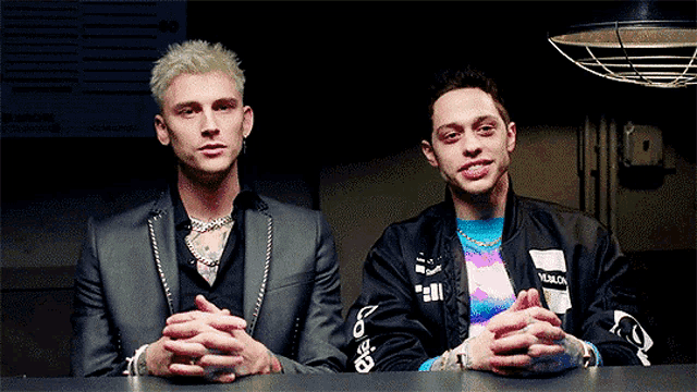 two men are sitting at a table with their hands folded and one of them is wearing a jacket that says vans on the sleeve