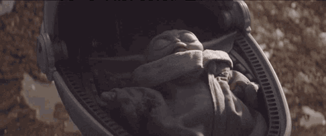 a baby yoda is sleeping in a stroller on the ground