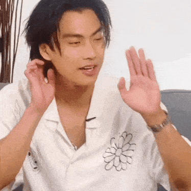 a young man wearing a white shirt with a flower on the front is waving his hand .