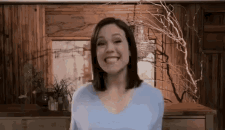 a woman in a blue shirt is smiling in front of a wooden wall in a living room .