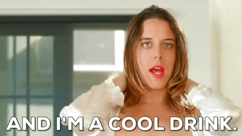 a woman is standing in front of a window and says `` and i 'm a cool drink . ''