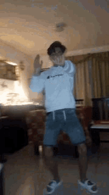 a man is dancing in a living room while wearing shorts and a white sweatshirt .