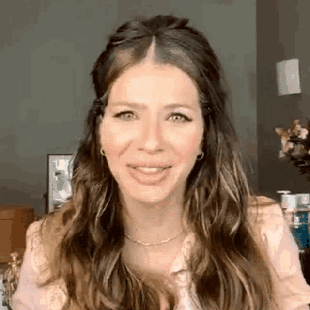 a woman with long hair is smiling and looking at the camera while wearing a pink shirt .