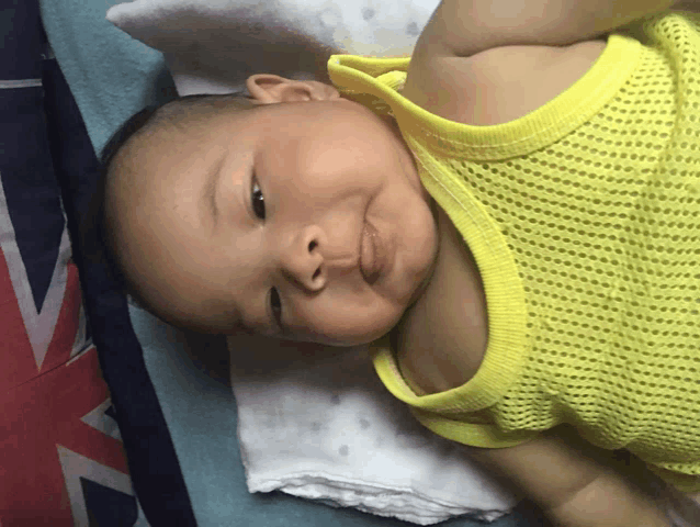 a baby wearing a yellow tank top is laying down on a bed