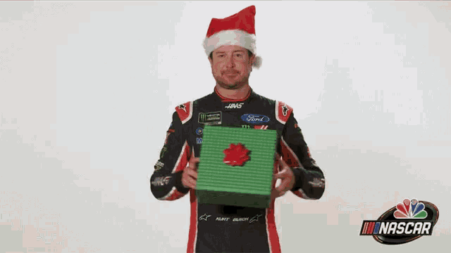 a race car driver wearing a santa hat is holding a green gift box .