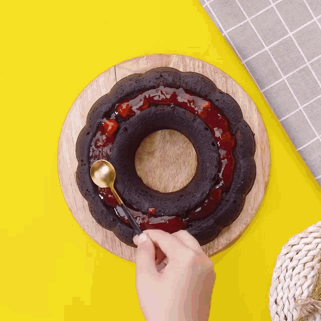 a person is spreading strawberry jam on a cake