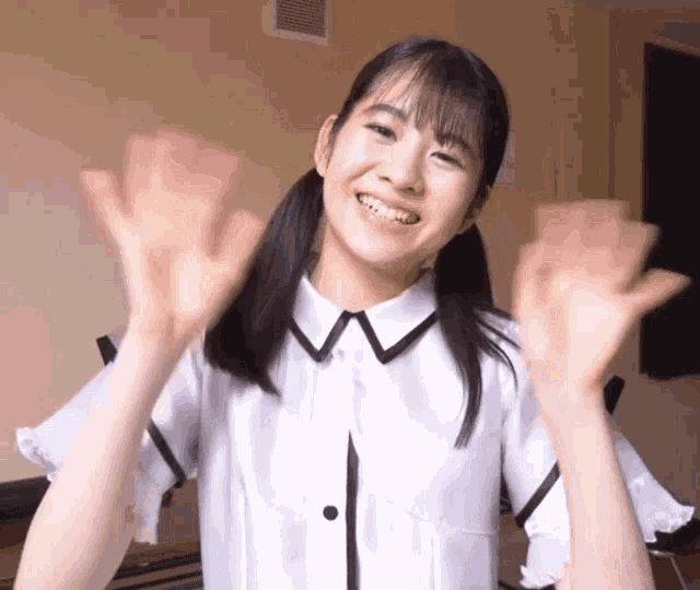 a girl in a white shirt is smiling with her hands up