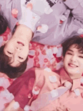 two men are laying upside down on a bed with petals on them .