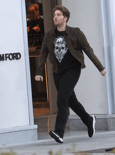 a man wearing a t-shirt with a skull on it is walking in front of a store called tom ford