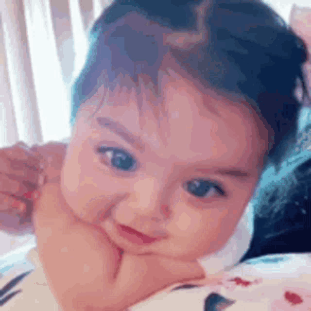 a baby girl is laying on a bed with her hand on her chin and smiling .