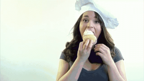 a woman wearing a chef hat is holding a cupcake with whipped cream on it