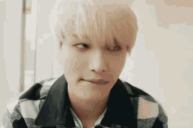 a young man with blonde hair is wearing a plaid jacket and making a funny face