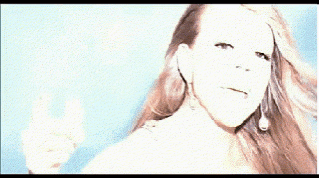 a woman wearing a necklace and earrings is smiling and waving her hand