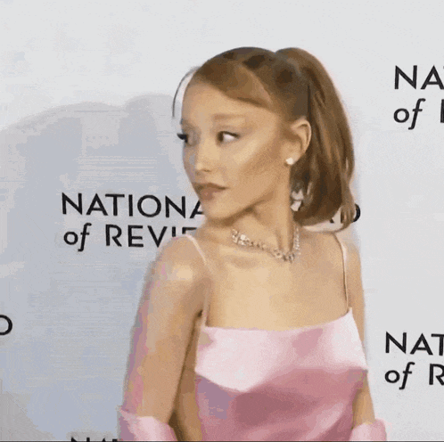 a woman in a pink dress is standing on a red carpet at the national review awards .