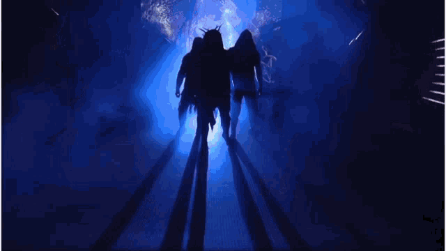 a group of men are standing in a dark room with a blue light behind them