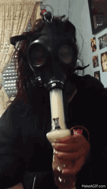 a woman wearing a gas mask is blowing a bong
