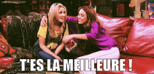 two women are sitting on a couch with the words t 'es la meilleure written on the bottom .