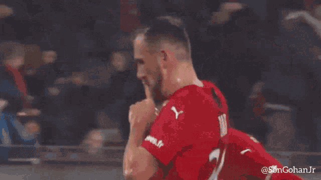 a soccer player wearing a red puma shirt holds his fist up