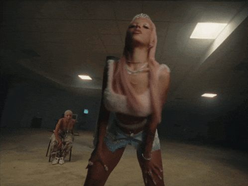 a woman in a pink wig is dancing with another woman in a wheelchair in the background