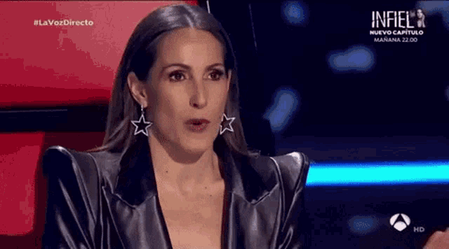 a woman wearing a black leather jacket and earrings is sitting in a chair on a stage .