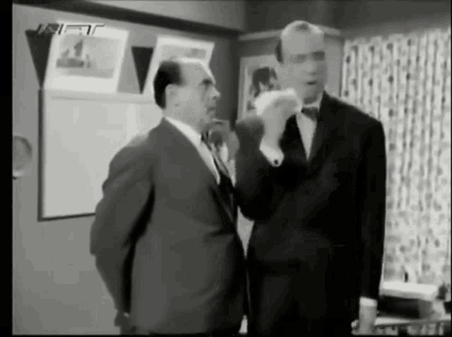 two men in suits and bow ties are standing next to each other in a room .