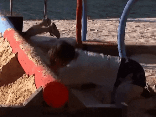 a person is laying on a sandbox with a red pipe in the background