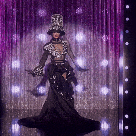 a woman in a long black dress is standing in front of a purple curtain of lights